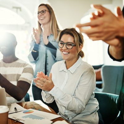 Diverse group of smiling business colleagues clapping together during a meeting while sitting in a modern office